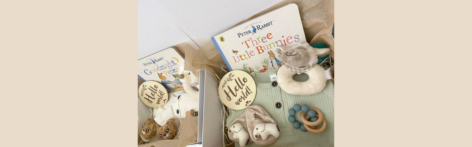 New baby hampers for a baby boy or girl, including a beige romper, plush animal rattle, silicone pacifier clip, hello world plaque and a Beatrix Potter Peter Rabbit storybook.