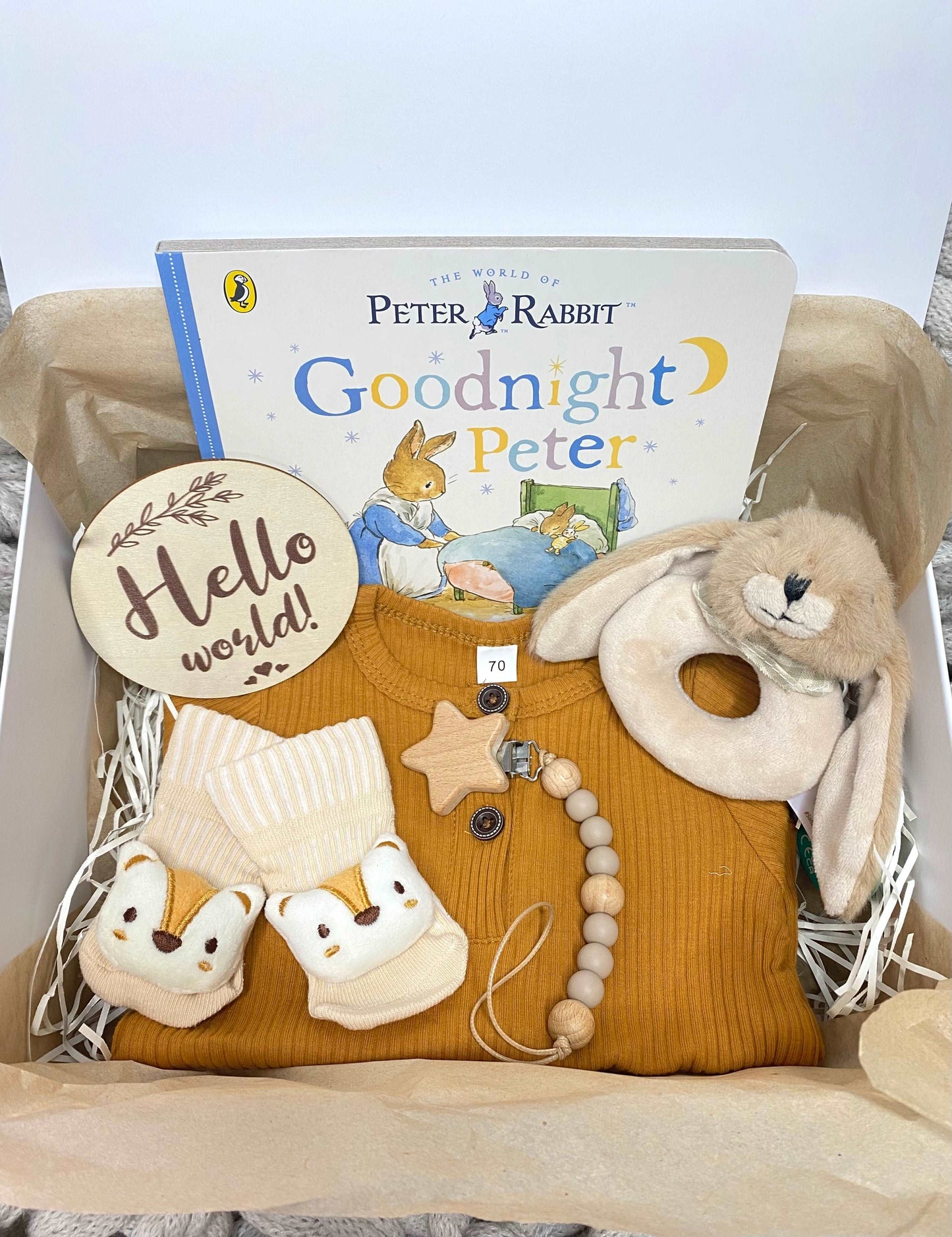 A new baby hamper for a baby boy or girl, including a pink romper, plush animal rattle, silicone teether, hello world plaque and a Beatrix Potter Peter Rabbit storybook. A prefect babygift