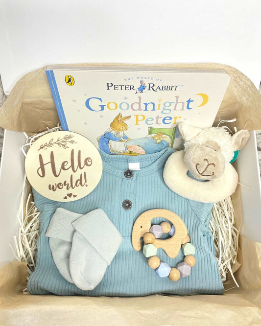 A new baby hamper for a baby boy, including a pink romper, plush animal rattle, silicone teether, hello world plaque and a Beatrix Potter Peter Rabbit storybook. A prefect babygift