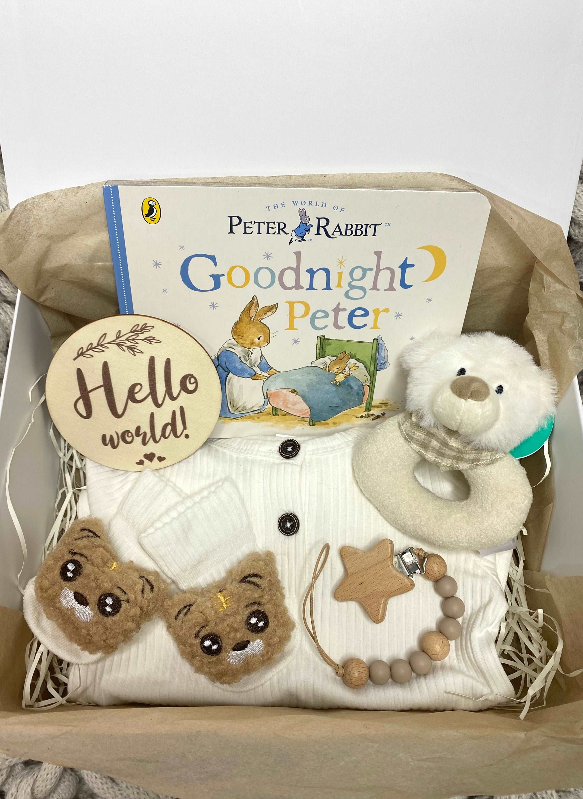 A new baby hamper for a baby boy or girl, including a pink romper, plush animal rattle, silicone teether, hello world plaque and a Beatrix Potter Peter Rabbit storybook. A prefect babygift