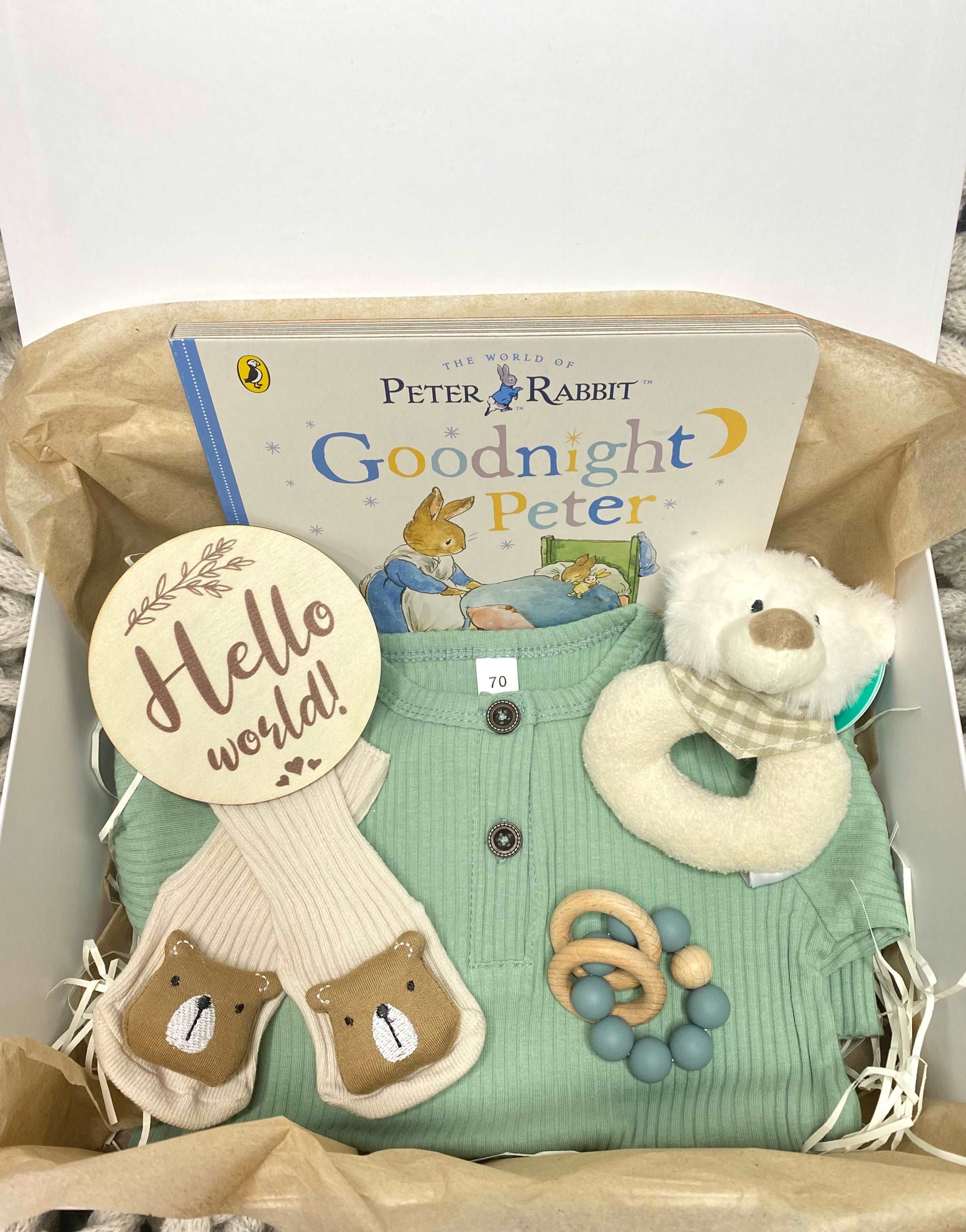 A new baby hamper for a baby boy or girl, including a pink romper, plush animal rattle, silicone teether, hello world plaque and a Beatrix Potter Peter Rabbit storybook. A prefect babygift