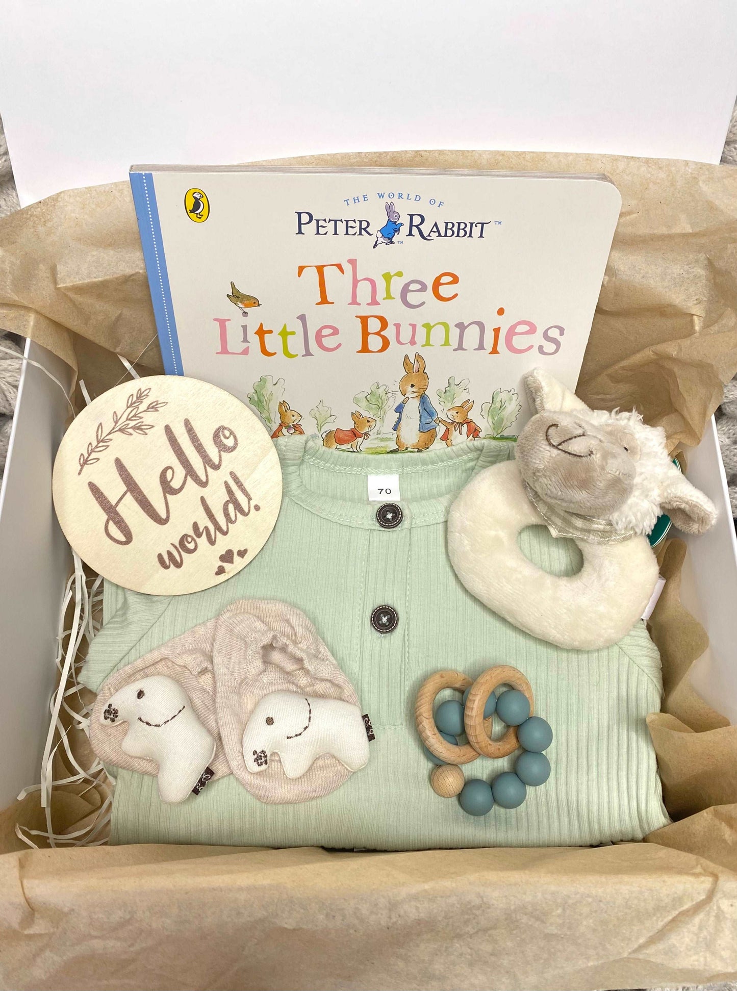 A new baby hamper for a baby boy or girl, including a pink romper, plush animal rattle, silicone teether, hello world plaque and a Beatrix Potter Peter Rabbit storybook. A prefect babygift