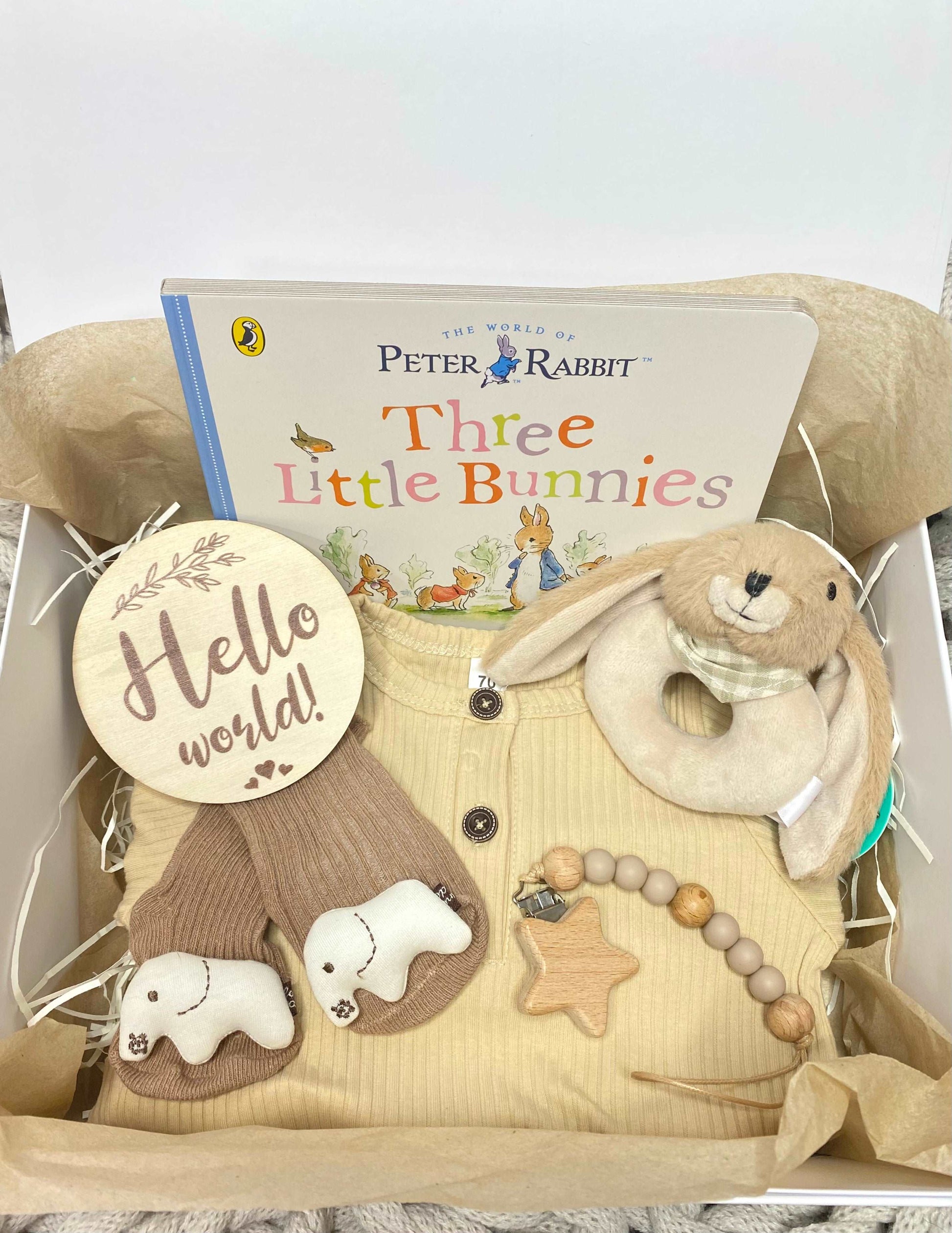 A new baby hamper for a baby boy or girl, including a pink romper, plush animal rattle, silicone teether, hello world plaque and a Beatrix Potter Peter Rabbit storybook. A prefect babygift