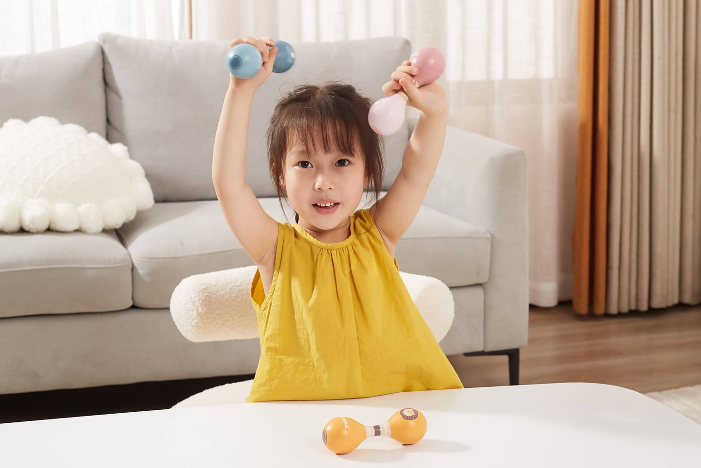 A child playing with wooden toy maracas made by PolarB, featuring two rounded ends connected by a striped handle. The maraca has the PolarB logo and a small animal illustration on one end.